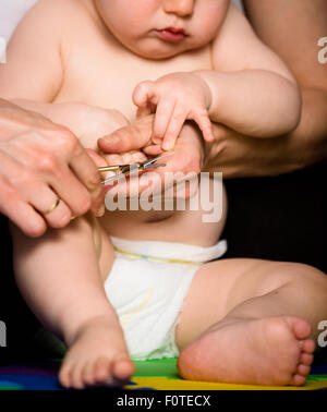 Mother cutting nails on hands of her baby - sitting on floor in bathroom Stock Photo