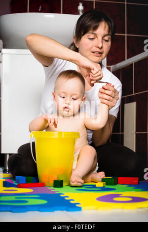 Mother cutting fingernails of her child while baby is playing with toys Stock Photo