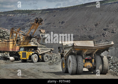 Excavator loading iron ore into heavy dump trucks on the opencast mining site Stock Photo