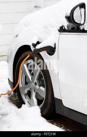 Electric car plugged in to an outlet recharging outdoors in winter snow Stock Photo