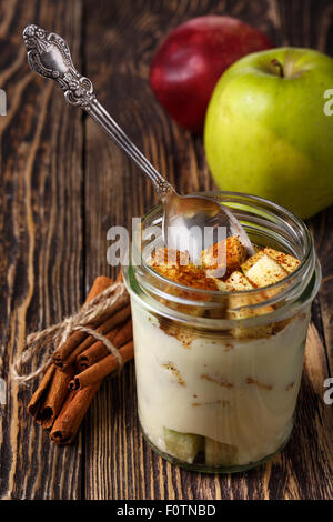 Parfait-style healthy layered snack or dessert with yogurt and apple with ground cinnamon in  glass on wooden table. Stock Photo