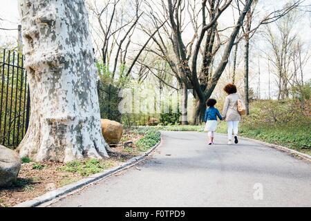 Rear view of mother and daughter walking along pathway holding hands Stock Photo