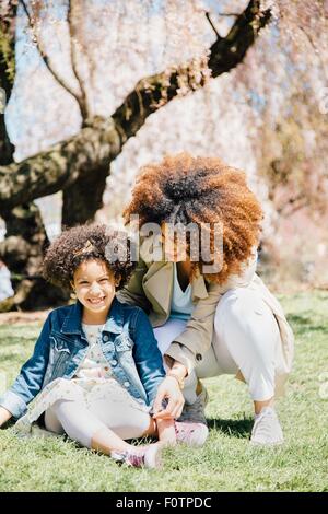 Mother crouching tending to daughter sitting on grass Stock Photo