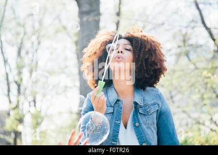 Front view of mid adult woman blowing bubbles, eyes closed, looking up