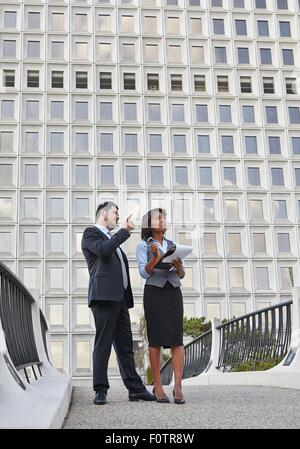 Business people standing talking holding paperwork, pointing and looking upwards Stock Photo