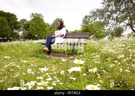 Mature woman sitting on bench in daisy filled park Stock Photo