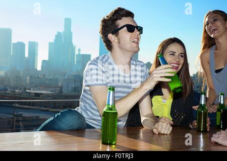 Young women and man drinking beer and laughing at rooftop bar with Los Angeles skyline, USA Stock Photo