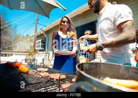 Mid adult man serving barbecue food to family in garden Stock Photo