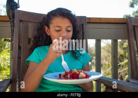Girl eating fruit dessert on garden bench Stock Photo