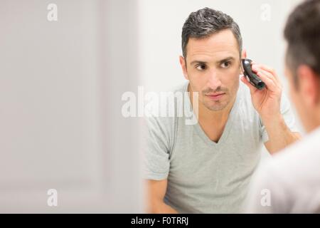 Mid adult man, looking in mirror, using electric shaver Stock Photo