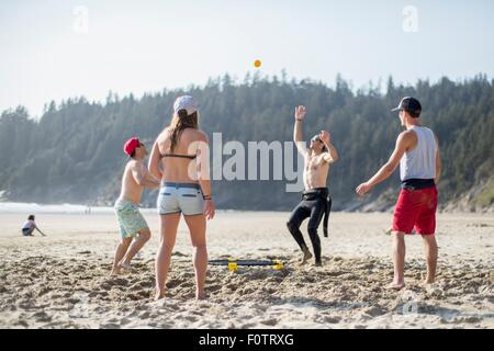 Four adult friends throwing and catching ball on Short Sands Beach, Oregon, USA Stock Photo