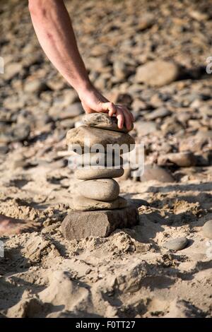 Hand of young man placing stone on stone stack at beach Stock Photo