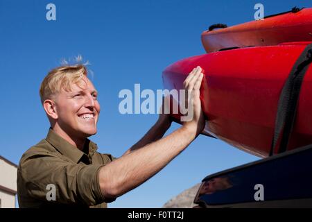 Portrait of young man unloading kayak, looking away smiling Stock Photo