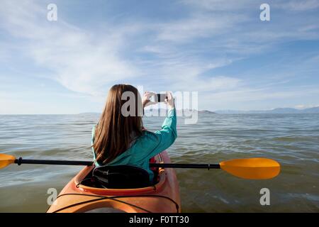 Rear view of young woman in kayak taking photograph, Great Salt Lake, Utah, USA