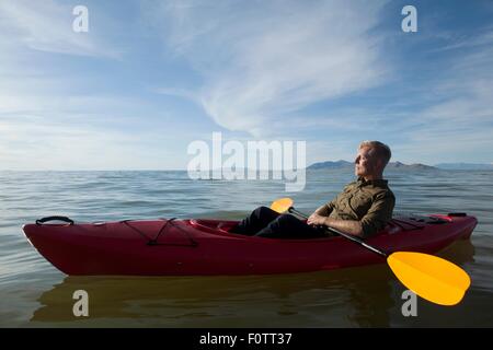 Side view of young man in kayak on water holding paddles, eyes closed, Great Salt Lake, Utah, USA Stock Photo