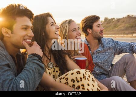 Group of friends sitting together on beach, at sunset Stock Photo