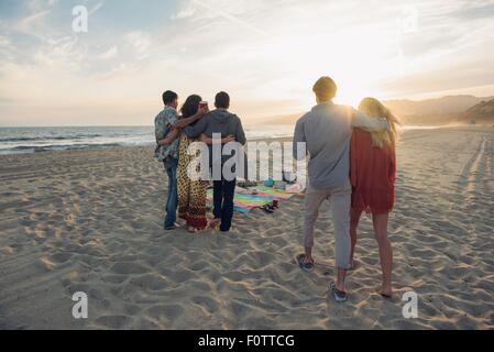 Group of friends standing on beach, hugging, rear view Stock Photo
