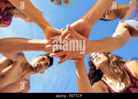 Group of friends joining hands on beach, low angle view Stock Photo