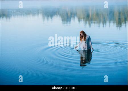 Young woman standing in middle of lake ripples looking down Stock Photo