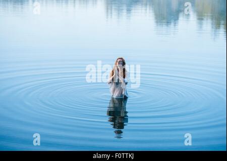 Young woman standing in lake ripples praying with eyes closed Stock Photo