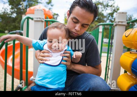 Young man guiding toddler brother on playground slide Stock Photo