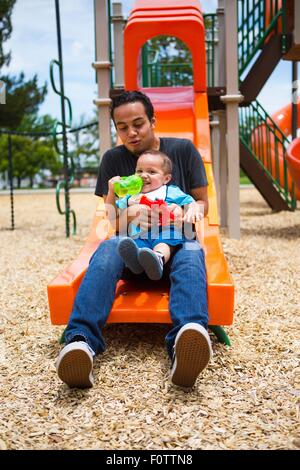 Young man with toddler brother on playground slide Stock Photo