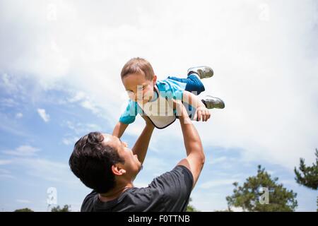 Young man playing lifting up toddler brother in park Stock Photo