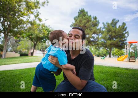 Male toddler kissing older adult brother in park Stock Photo