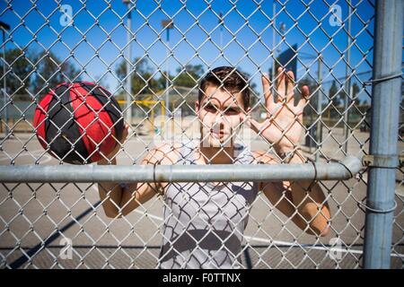 Portrait of young male basketball player behind basketball court fence Stock Photo