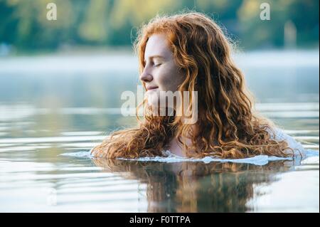 Head and shoulders of beautiful young woman with eyes closed in lake