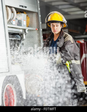 Confident Firewoman Spraying Water At Fire Station Stock Photo