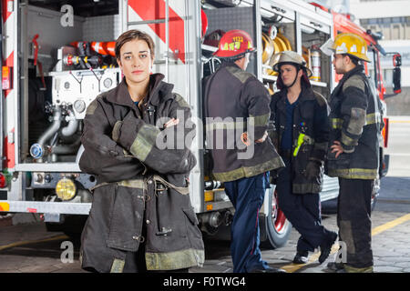 Confident Firewoman With Colleagues Standing By Truck Stock Photo