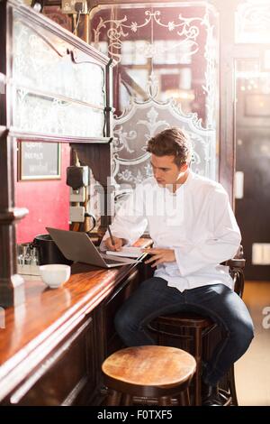 Young chef sitting on bar stool at work using laptop Stock Photo