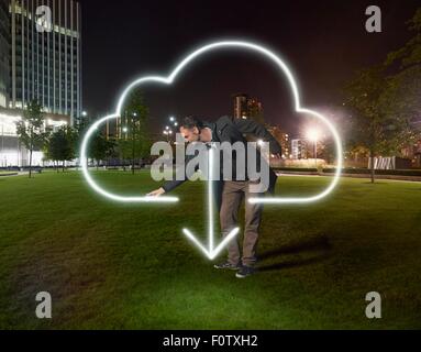 Artist painting cloud download symbol outside office building at night Stock Photo