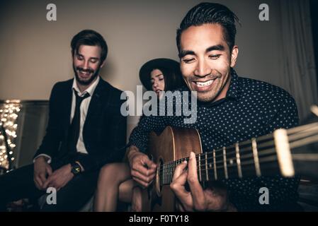Group of friends sitting on sofa, young man playing guitar Stock Photo