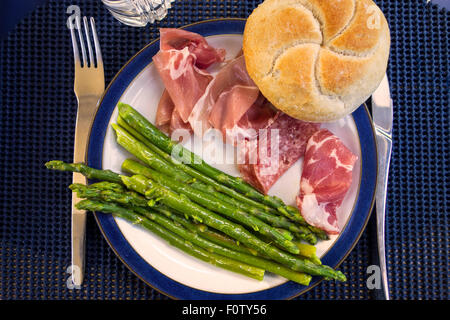 A plate of Italian antipasto meats ( prosciutto, salami  Milano, coppa) with asparagus and a bread roll Stock Photo