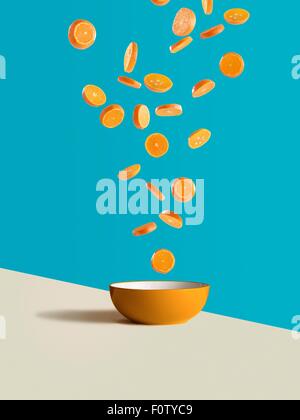 Fresh sliced oranges dropping into orange bowl Stock Photo