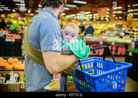 Father holding baby son and shopping basket in supermarket Stock Photo