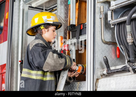 Female Firefighter Fixing Water Hose In Truck Stock Photo