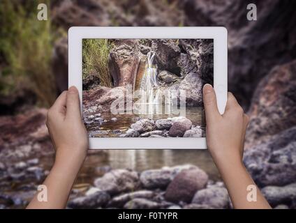 Hands of young woman holding up digital tablet with view of Samaria Gorge in front of view of Samaria Gorge, Crete, Greece Stock Photo