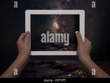 Hands of young woman holding up digital tablet with view of milky way in front of view of milky way at night, Crete, Greece Stock Photo