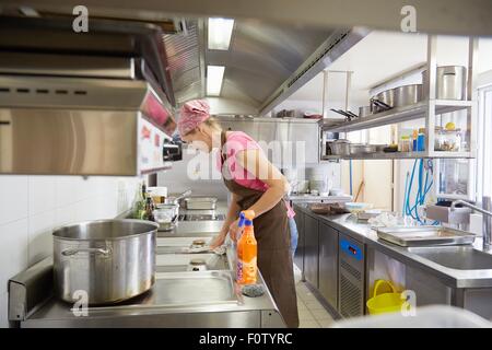 Mature woman wearing apron and headscarf cleaning kitchen hob Stock Photo