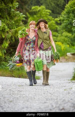 Two women carrying vegetables along rural road Stock Photo
