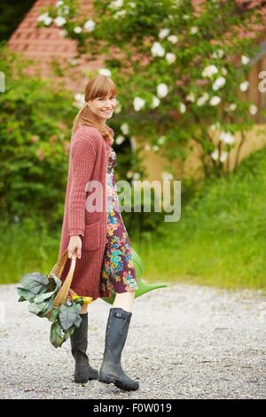 Portrait of woman carrying vegetables along rural road Stock Photo