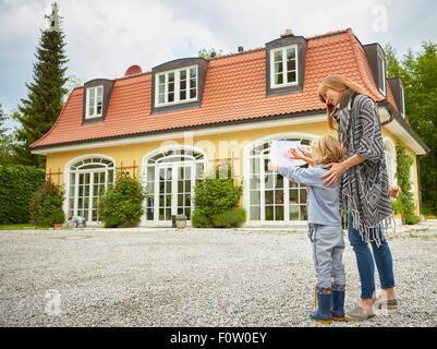 Boy showing mid adult woman crayon drawing, standing in front of house Stock Photo