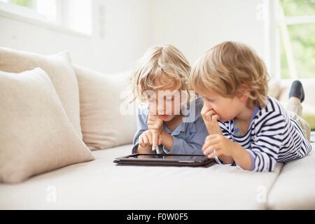 Two boys lying on fronts side by side on sofa using digital tablet Stock Photo