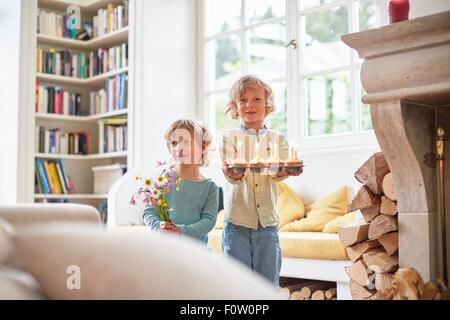 Two boys holding flowers and cupcakes with lit cndles Stock Photo