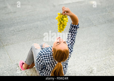 Young woman eating grapes outdoor sitting on stairs - above view Stock Photo