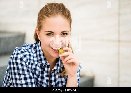 Young woman - teenage girl eating grapes outdoor sitting on stairs Stock Photo