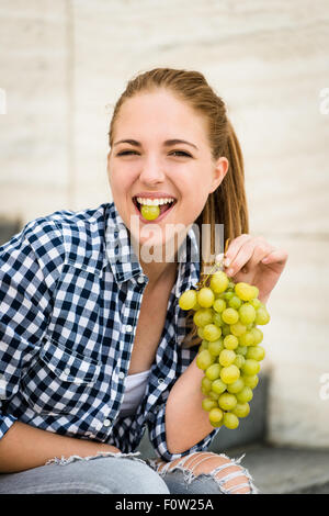 Young woman eating grapes outdoor - holding grape between teeth Stock Photo